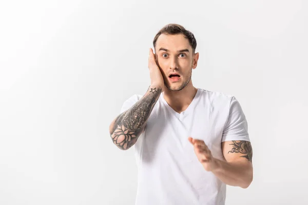 Chocado bonito jovem tatuado homem tocando rosto isolado no branco — Fotografia de Stock