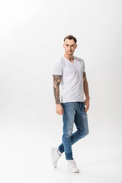 Longitud completa vista de guapo joven tatuado hombre posando aislado en blanco - foto de stock