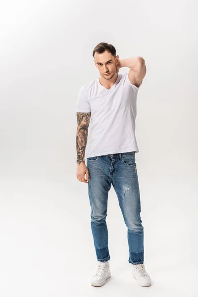 Longitud completa vista de guapo joven tatuado hombre posando aislado en blanco - foto de stock