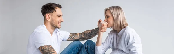 Young tattooed pregnant woman kissing husband hand isolated on grey, panoramic shot — Stock Photo