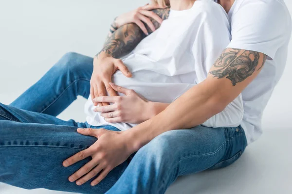 Vue recadrée de jeune femme enceinte tatouée assise près du mari sur gris — Photo de stock