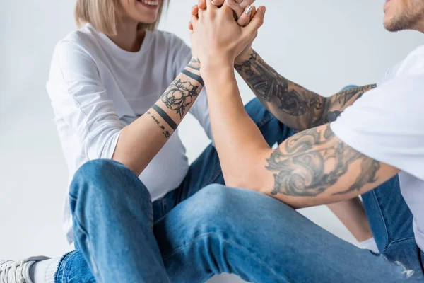 Corte vista de sorrir jovem tatuado grávida segurando as mãos com o marido isolado no cinza — Fotografia de Stock