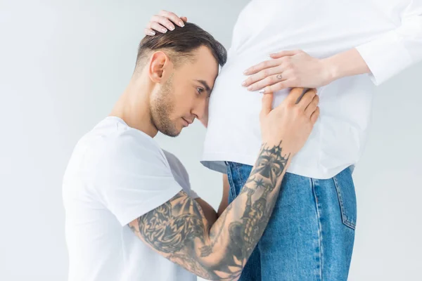 Seitenansicht eines jungen tätowierten Mannes, der Bauch einer schwangeren Frau berührt, isoliert auf grau — Stockfoto
