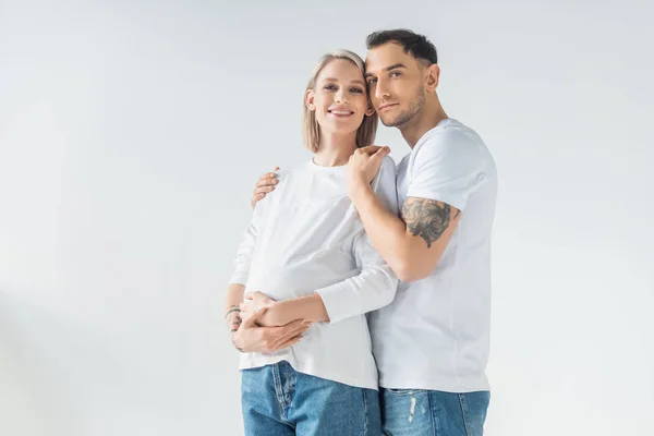 Happy young tattooed pregnant woman hugging with boyfriend isolated on grey — Stock Photo