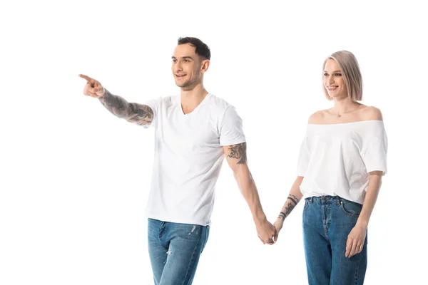 Young tattooed couple holding hands while man pointing with finger away isolated on white — Stock Photo