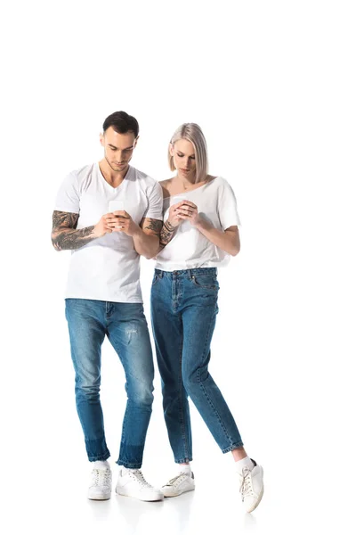 Joven pareja tatuada utilizando teléfonos inteligentes aislados en blanco - foto de stock