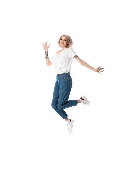 Full length view of happy blonde young tattooed girl jumping isolado no branco — Fotografia de Stock