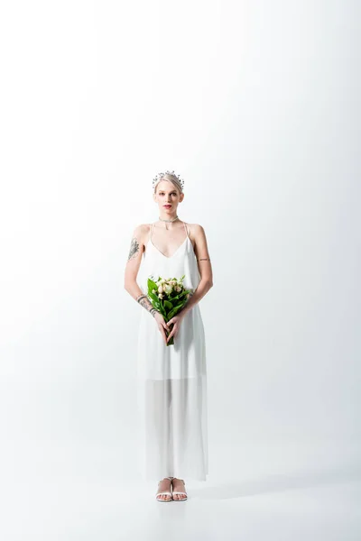Beautiful tattooed bride standing with floral bouquet on white — Stock Photo