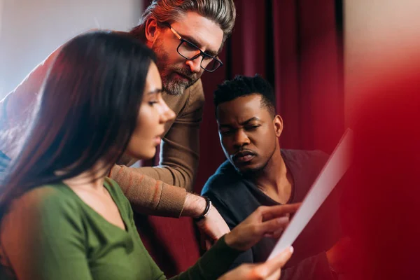 Multikultureller junger Schauspieler und Schauspielerin liest Drehbuch mit reifem Theaterregisseur — Stockfoto