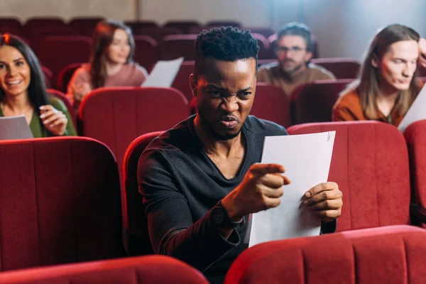 Angry african american actor rehearsing on red chairs with actors — стокове фото