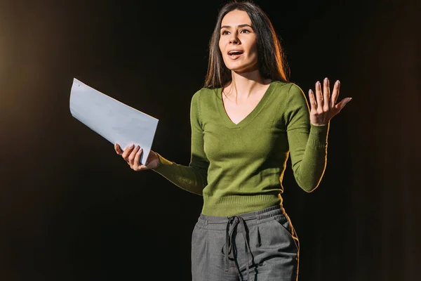 Beautiful emotional actress performing role with screenplay on black — Stock Photo