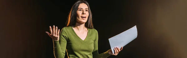 Panoramic shot of attractive young actress reading scenario on black — Stock Photo