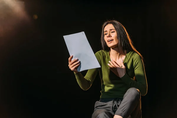 Attractive emotional actress reading scenario on black — Stock Photo