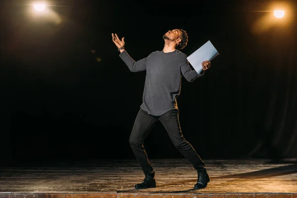Actor afroamericano sosteniendo escenario y de pie en el escenario durante el ensayo en el teatro - foto de stock