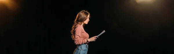 Panoramic shot of attractive young actress reading scenario on black — Stock Photo