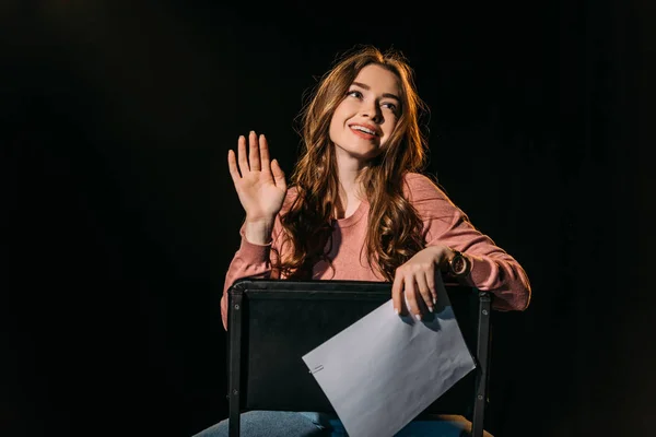 Жизнерадостная молодая актриса со сценарием, сидящая на стуле в театре — стоковое фото