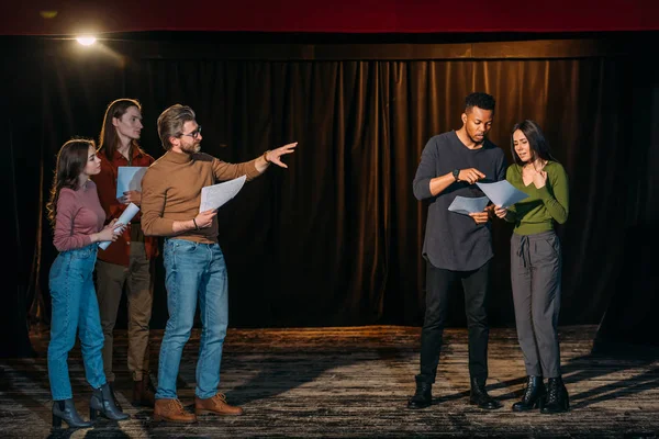 Jóvenes actores multiétnicos y actrices ensayando con el director de teatro maduro en el escenario - foto de stock