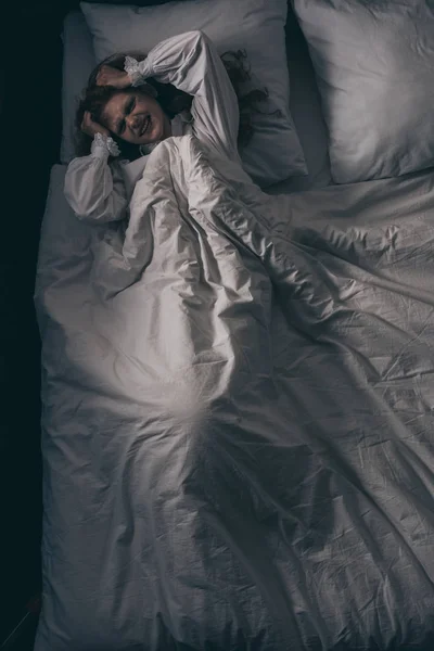 Vista superior da menina paranormal em camisola com dor de cabeça deitada na cama — Fotografia de Stock