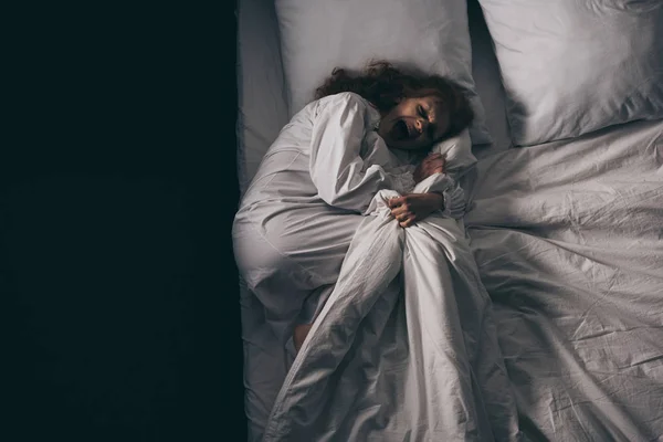 Вид сверху на одержимую женщину в ночном халате, кричащую, лежа в постели — стоковое фото