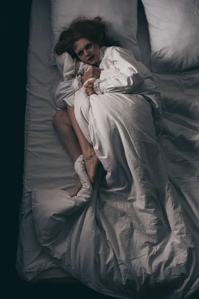 Вид зверху паранормальної дівчини в нічній сукні лежить в ліжку — стокове фото
