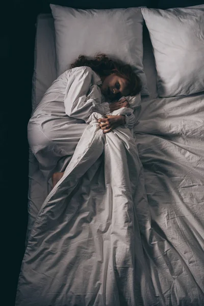 Vista dall'alto della ragazza ossessionata in camicia da notte sdraiata a letto — Foto stock