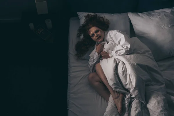 Вид сверху на демоническую женщину в ночном халате, лежащую в постели — стоковое фото
