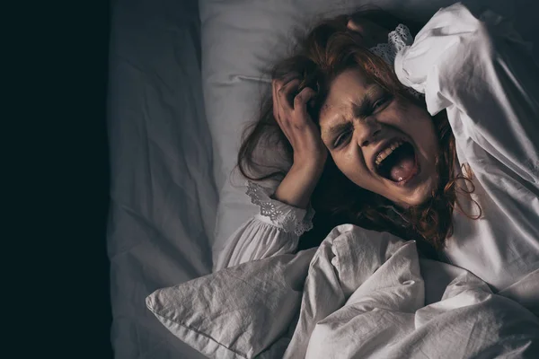 Вид сверху одержимой девушки в ночном халате, кричащей, лежа в постели — стоковое фото