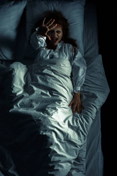 Vue du haut de la fille maléfique en chemise de nuit crier et gesticuler tout en étant couché dans le lit — Photo de stock