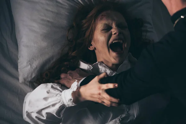 Exorcist holding yelling female demon in bed — Stock Photo