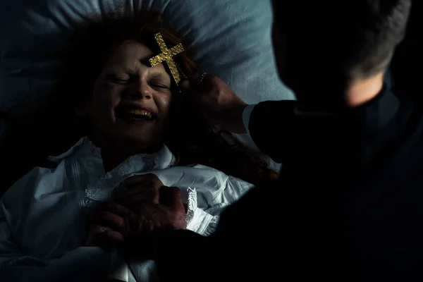 Экзорцист держит крест над смеющимся демоном в постели — стоковое фото