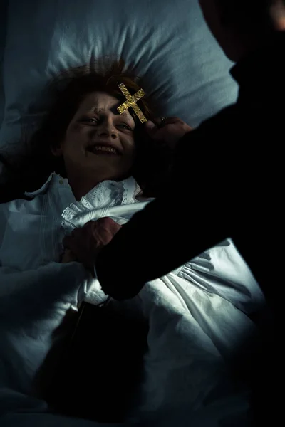 Exorzist hält Kreuz über weiblichen Dämon im Bett — Stockfoto