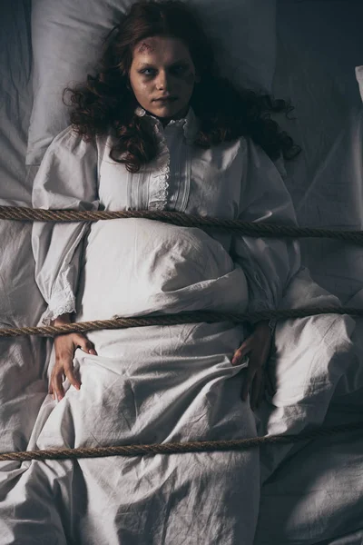 Одержимая девушка в ночной рубашке, связанная веревкой в постели — стоковое фото