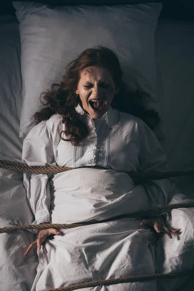Demonic obsessed yelling girl in nightgown bound with rope in bed — Stock Photo