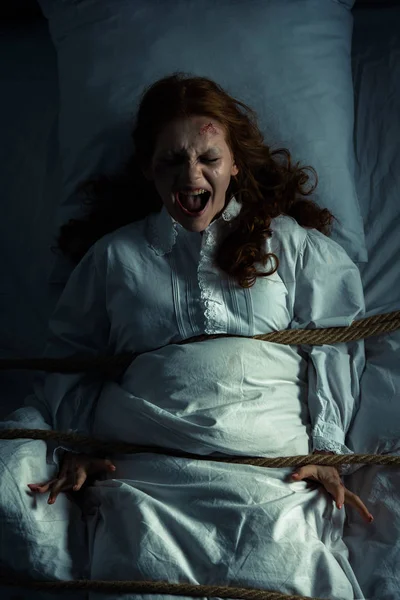 Femmina urlando demone in camicia da notte legato con corda a letto — Stock Photo