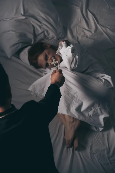 Экзорцист держит крест над женщиной-демоном в постели — стоковое фото