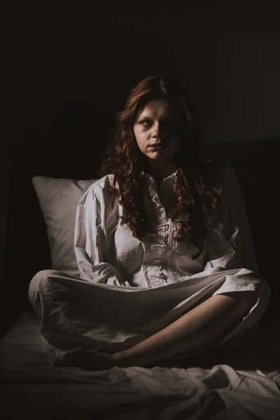 Demonic young woman in nightgown sitting in bed — Stock Photo