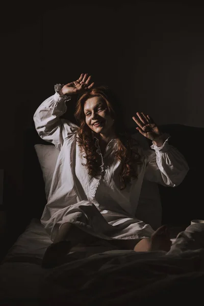 Terrível obcecado sorrindo menina em camisola sentada na cama — Fotografia de Stock