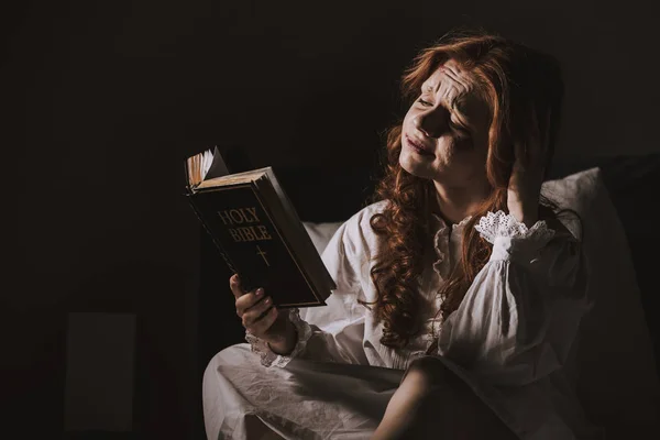 Creepy demoniacal crying woman reading holy bible on bed — Stock Photo