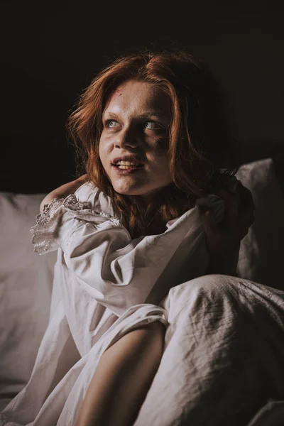 Demonic smiling girl in nightgown sitting in bed — Stock Photo