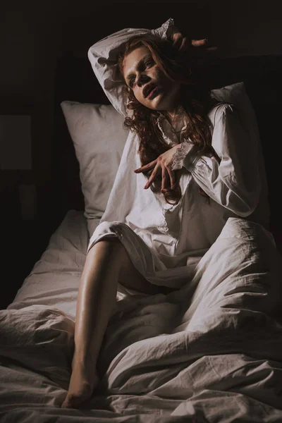 Paranormale ossessionato giovane donna in camicia da notte seduta a letto — Foto stock