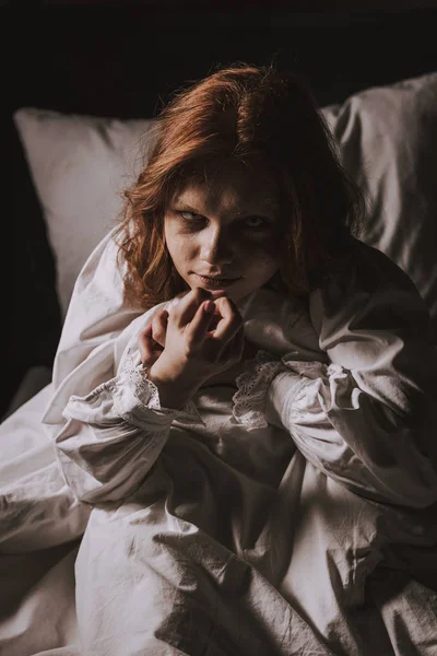 Paranormal demoniacal girl in nightgown sitting in bed — Stock Photo
