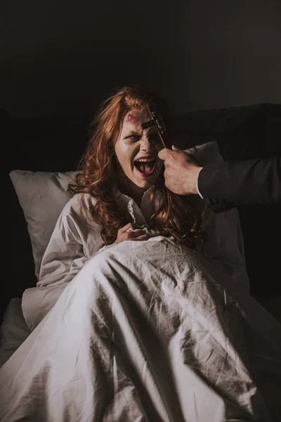 Exorcist holding cross in front of obsessed yelling girl in bed — Stock Photo