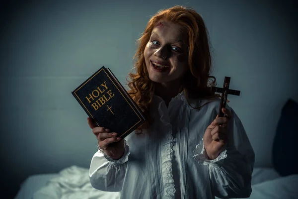 Smiling demoniacal woman holding cross and holy bible — Stock Photo