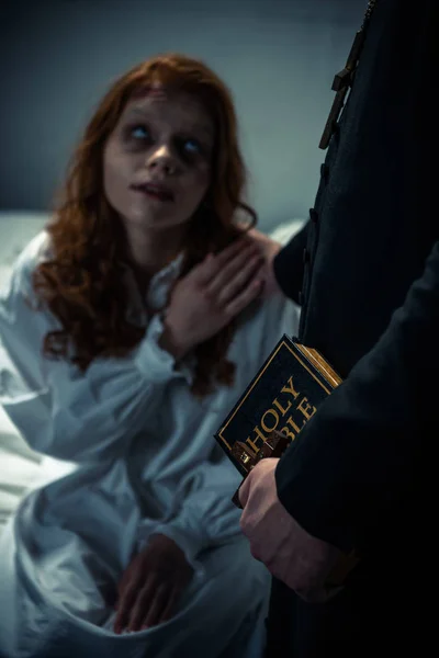 Экзорцист с библией, держащийся за руки с демонической девушкой в спальне — стоковое фото