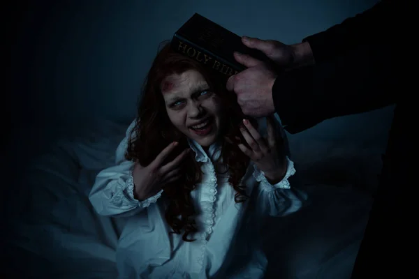Exorcista segurando bíblia perto da cabeça da menina obcecada no quarto — Fotografia de Stock