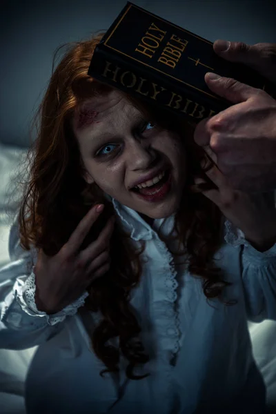 Экзорцист держит библию рядом с одержимой демонической девушкой в спальне — стоковое фото