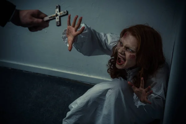 Exorcista sosteniendo cruz delante de gritando chica obsesionada - foto de stock