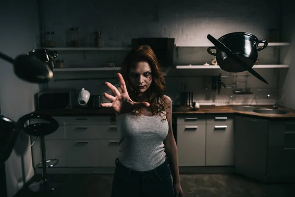 Concentrated demoniacal girl with levitating kitchenware in kitchen — Stock Photo