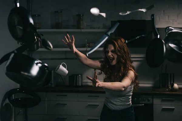 Creepy yelling girl gesturing with levitating kitchenware in kitchen — Stock Photo