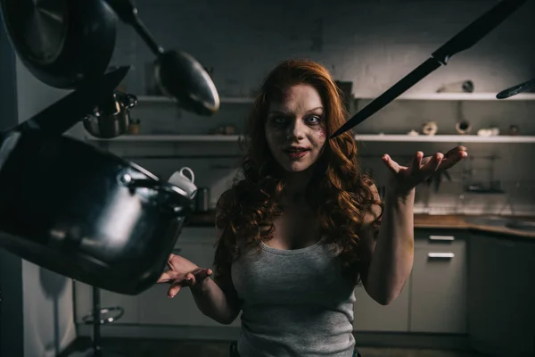 Creepy demoniacal girl with levitating kitchenware in kitchen — Stock Photo